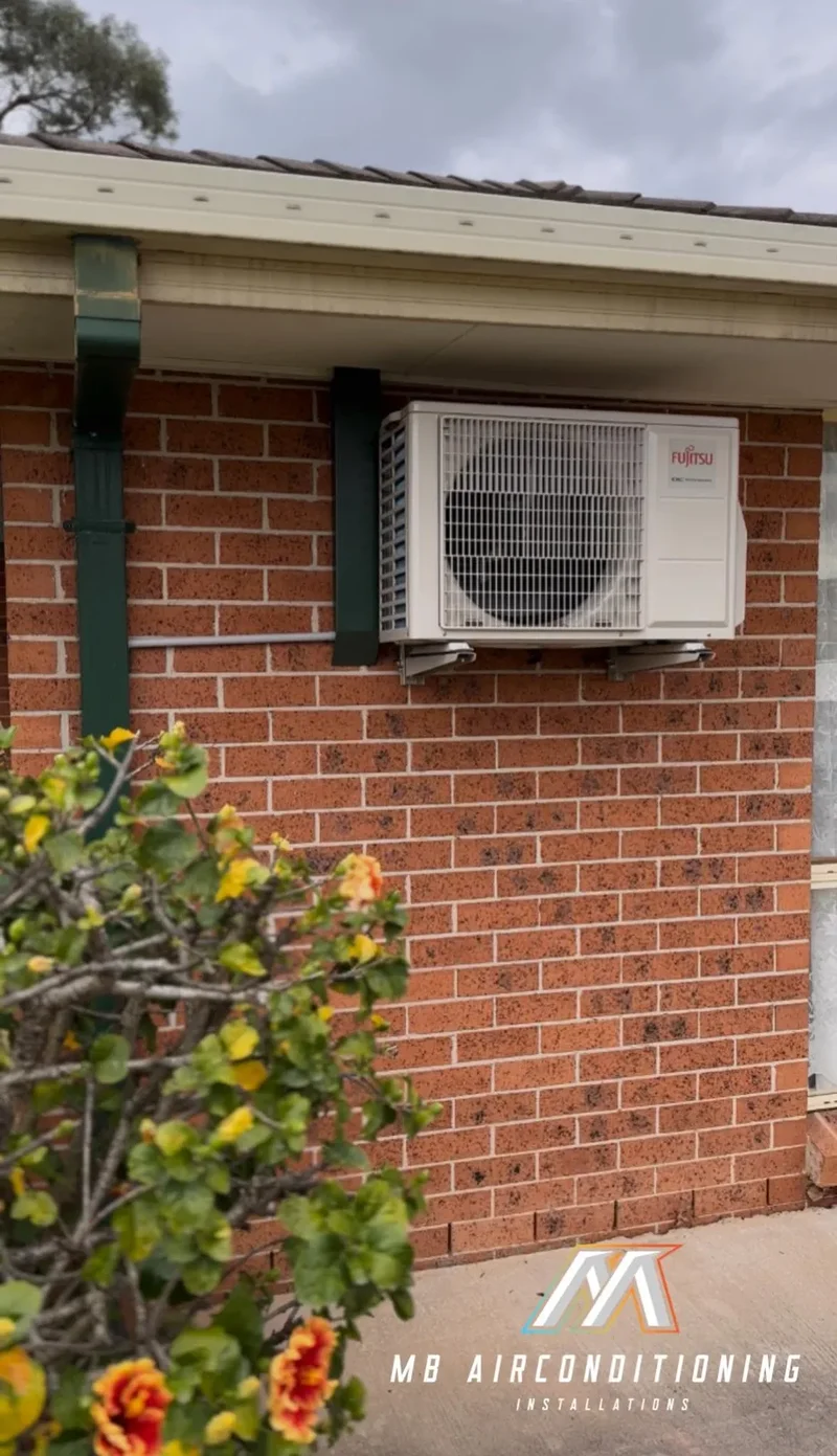 Reverse cycle outdoor condenser mounted on a brick wall beside a garden